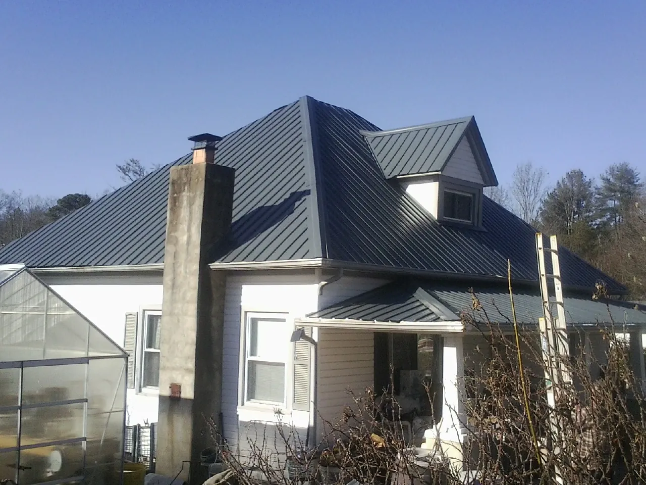 Dark blue standing seam metal roof on a white farmhouse with dormer — Slate & Tile Roof Repair by Roofing Brothers in Kenesaw