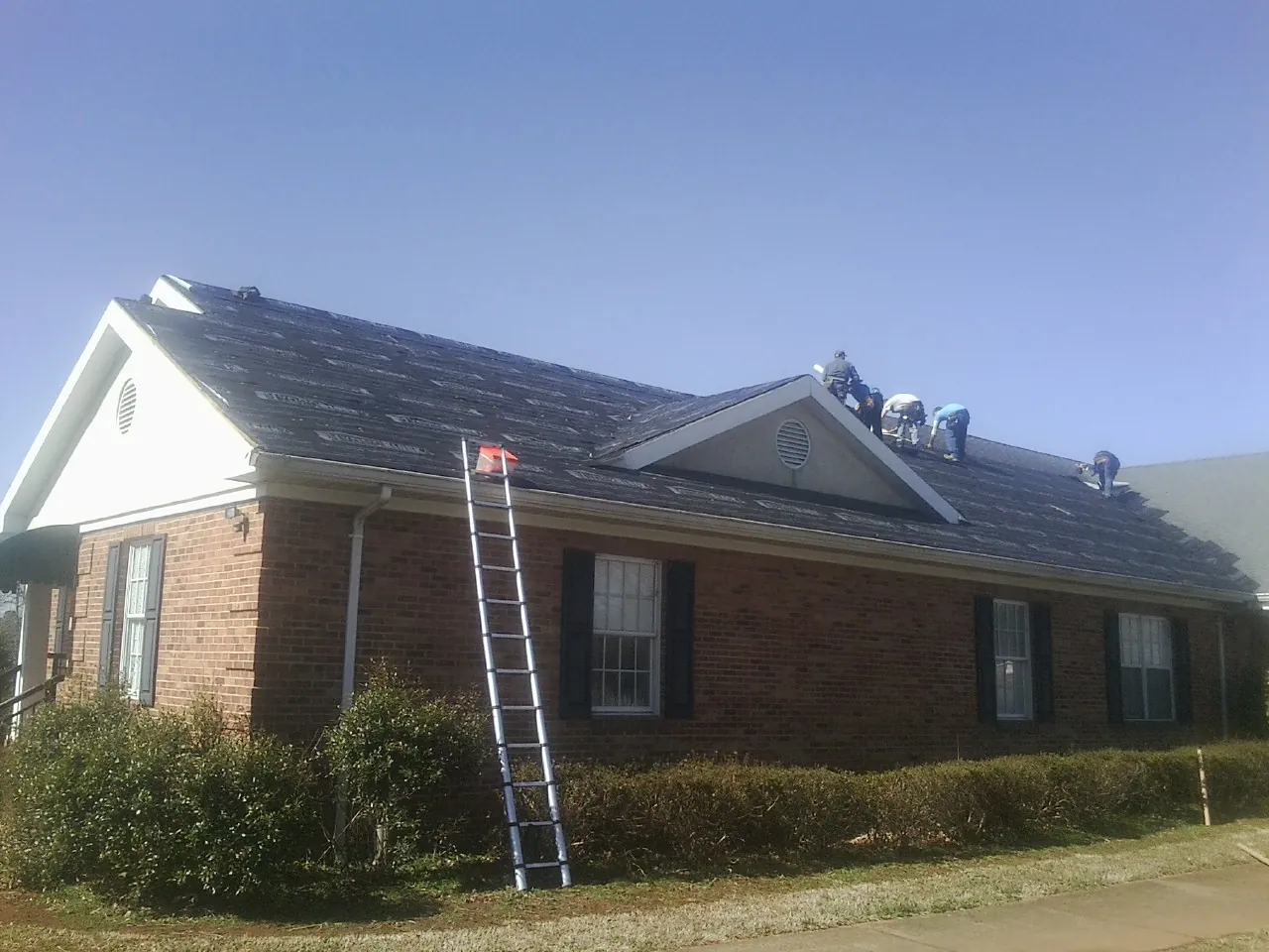Crew tearing shingles off a brick ranch roof with a ladder set — Emergency Roof Repair work by our crew in Kenesaw