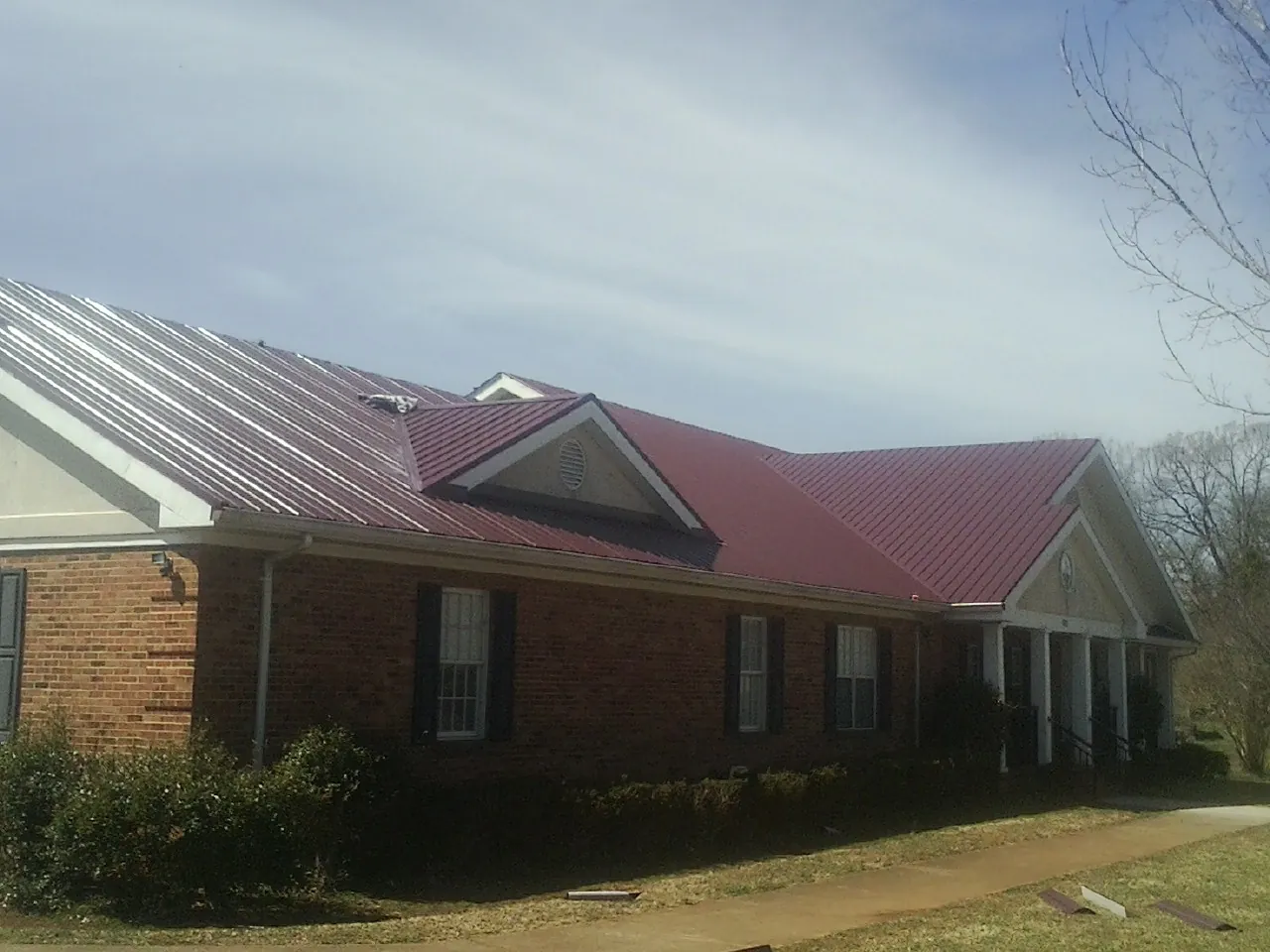Red metal roof with gabled entries on a long brick building, from a Hail Damage Roof Repair job in Kenesaw