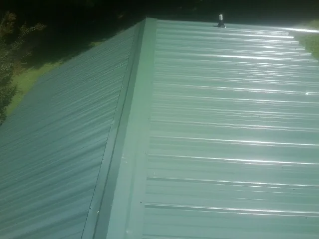 New green metal panels meeting at the ridge of a roof — Flat Roof Repair work by our crew in Kenesaw