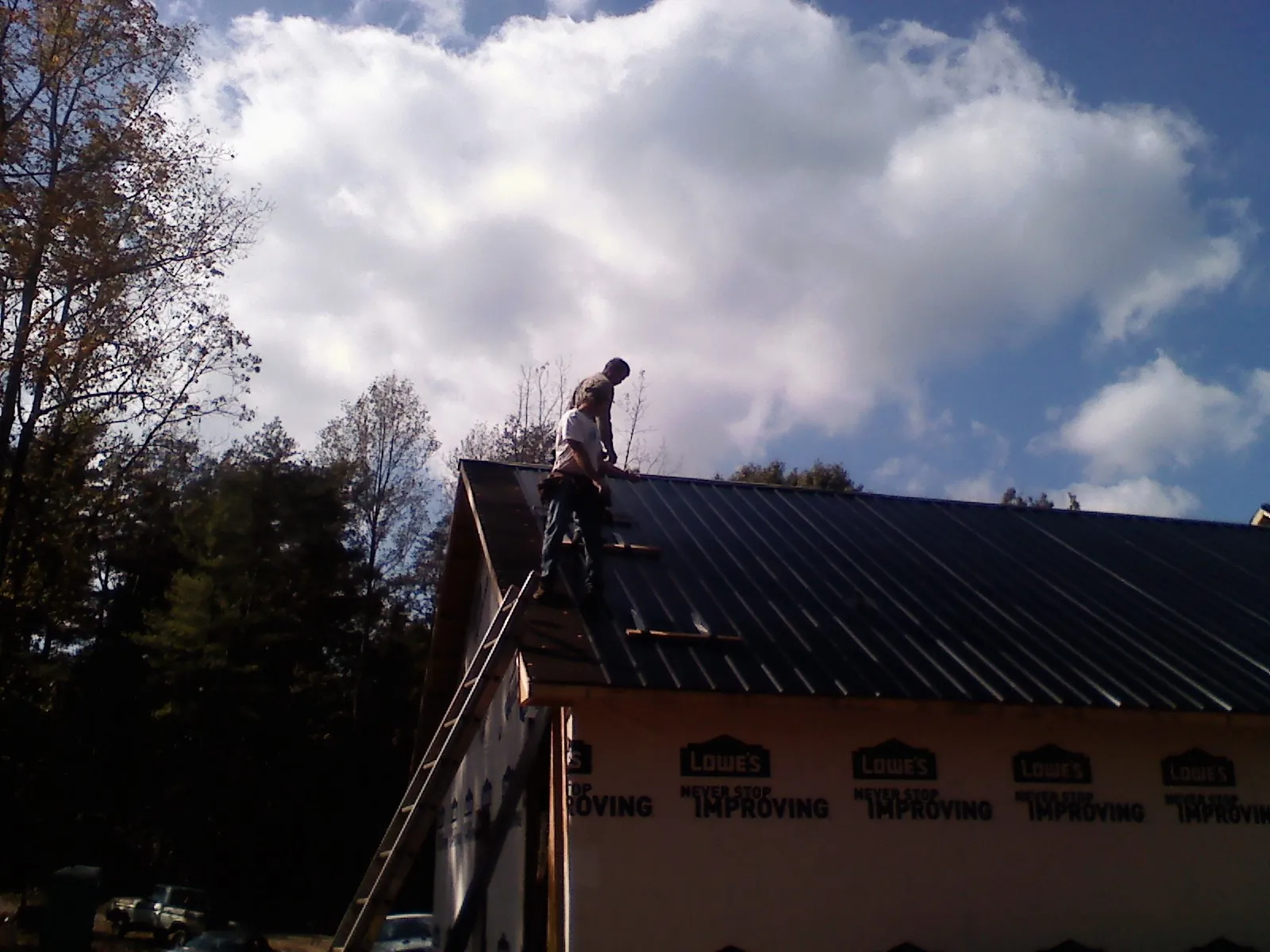 Roofer fastening dark metal panels high against a cloudy sky, from a Roof Inspection job in Kenesaw