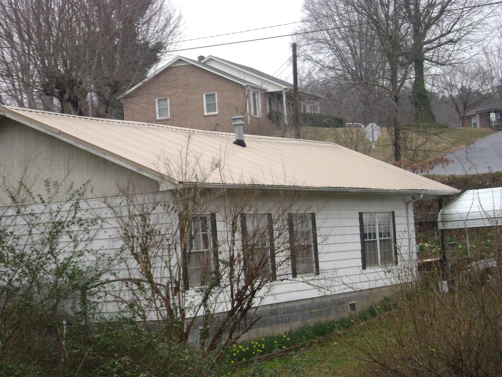 Tan metal roof on a white sided house set into a hillside — Commercial Roofing by Roofing Brothers in Kenesaw